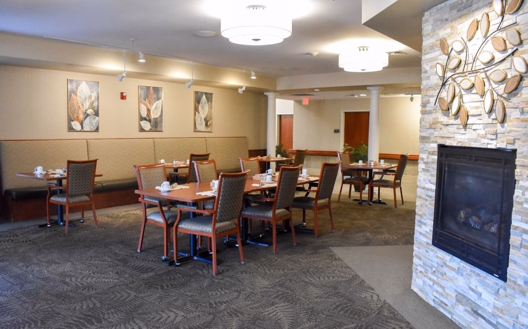A wider angle of the Grapevine café at Willow Brook Home in Columbus, Ohio, where comfortable seating and a cozy fireplace welcome residents to a casual dining experience.